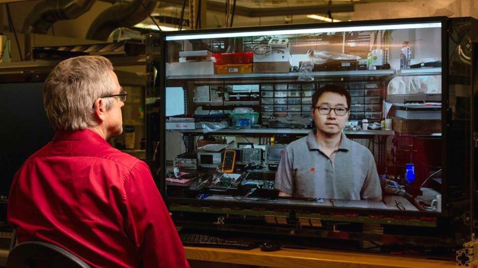 Two researchers conversing by way of displays with embedded cameras