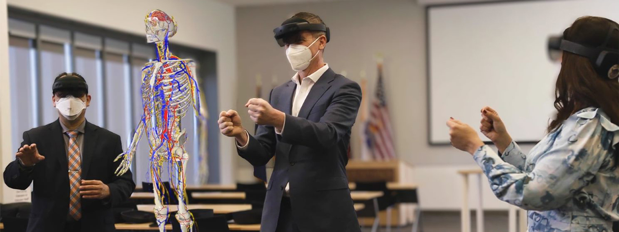 3 business professionals use mixed-reality headsets in a classroom to collaborate on viewing a virtual reality skeleton