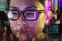 Zoomed in photo of a woman wearing glasses with a computer screen reflected in her lenses.