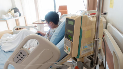 A child reclines in a hospital bed while in the foreground medical monitoring equipment shows digital readouts