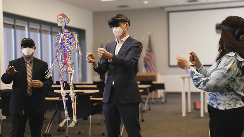 3 business professionals use mixed-reality headsets in a classroom to collaborate on a virtual reality skeleton