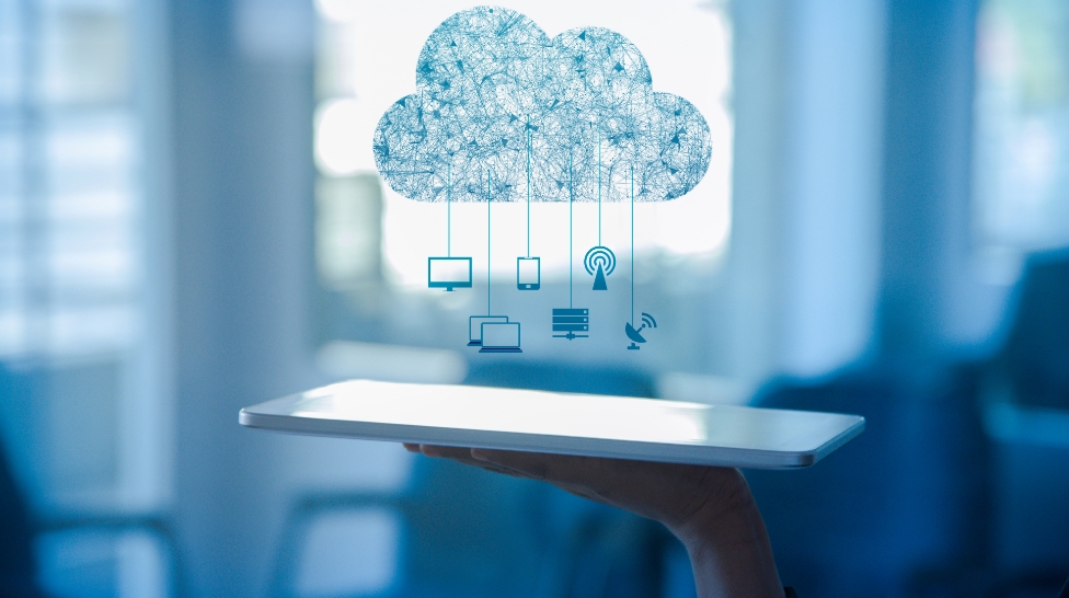 a tablet rests flat on the palm of a worker with a devices connected cloud graphic floating over top of the tablet