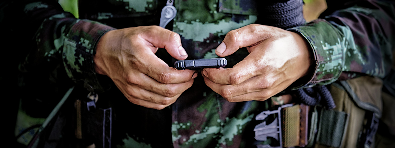 Close up shot of the hands of a man in military uniform typing on a smartphone device