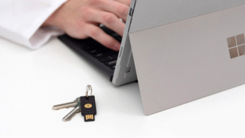 hands typing on a Microsoft table next to a YubiKey