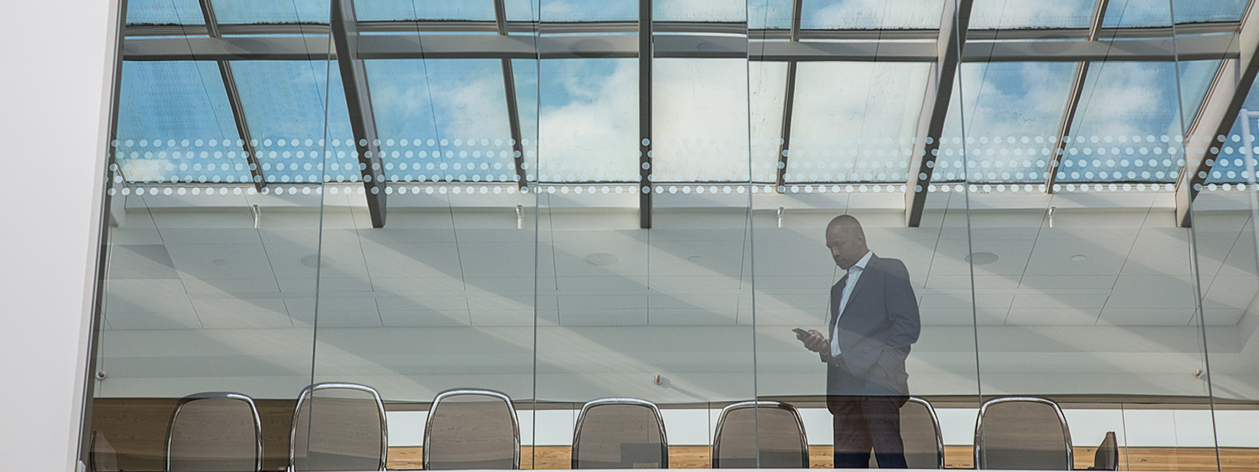 Businessman standing near the windows in a conference room, looking at phone