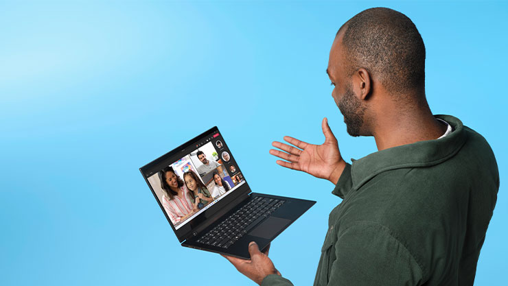 Photograph of adult male on blue studio background using Lenovo Yoga Slim 7 to enjoy a Microsoft Teams call with several participants.