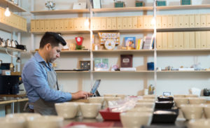 Image of a bakery owner and operator working on his laptop amid bowls and coffee cups.