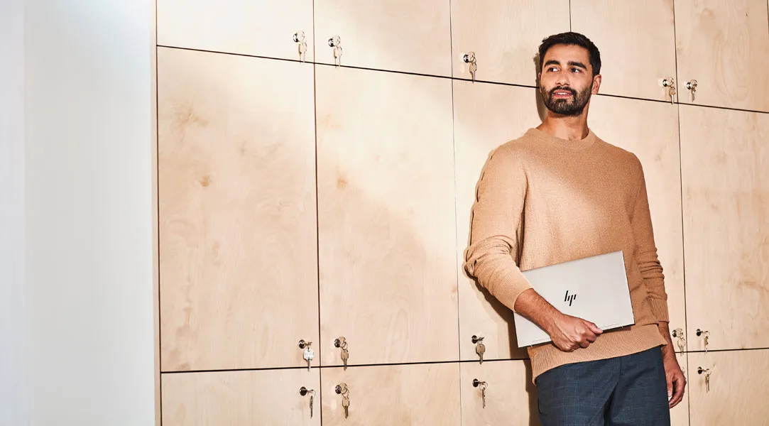 Ein Mann mit Laptop im Arm lehnt an Wand mit Aufbewahrungsboxen.