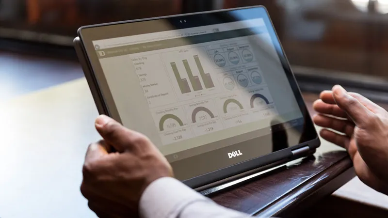 Nahaufnahme der Hände eines Mannes mit Tablet in einem Café-Restaurant. Der Bildschirm zeigt Diagramme der Verkäufe, Spar- und Girokonten der TD Bank.