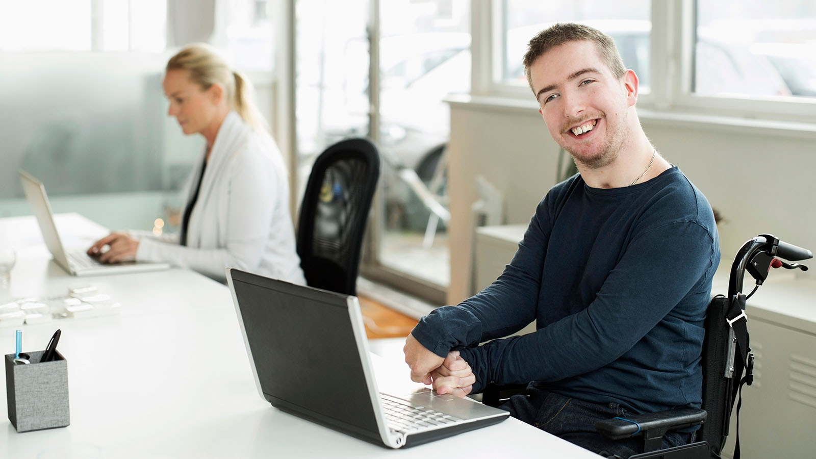 Porträt eines lächelnden Geschäftsmannes mit Cerebralparese, der ein Laptop im Büro verwendet.