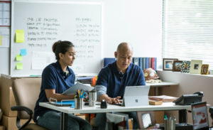 Image of two firstline workers sitting behind a desk making plans on their laptops.