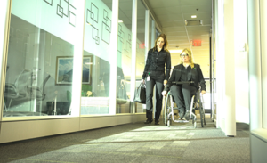 Image of two workers chatting in an accessible workplace hallway, one standing, the other from a wheelchair.