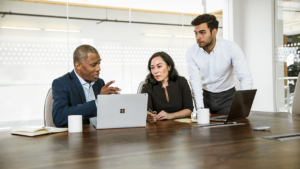 Image of three workers in a conference room gathered around a tablet.