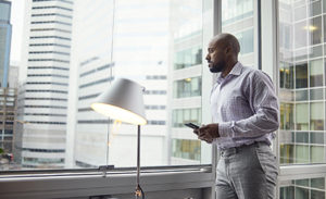 Image of a worker looking up from his phone to gaze out a window.