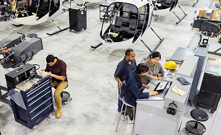 Image of workers assembling a helicopter. Several are gathered around a laptop.