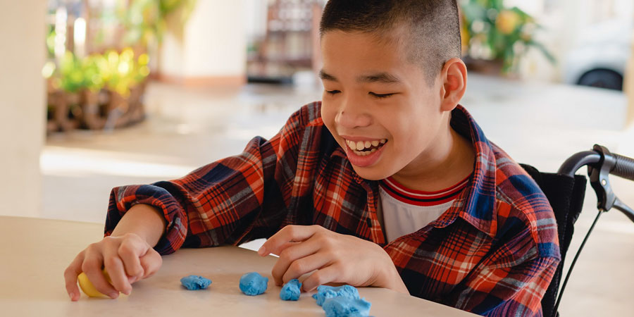 A smiling child plays with playdough at a desk