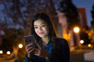 Female college student on campus at night, using phone.