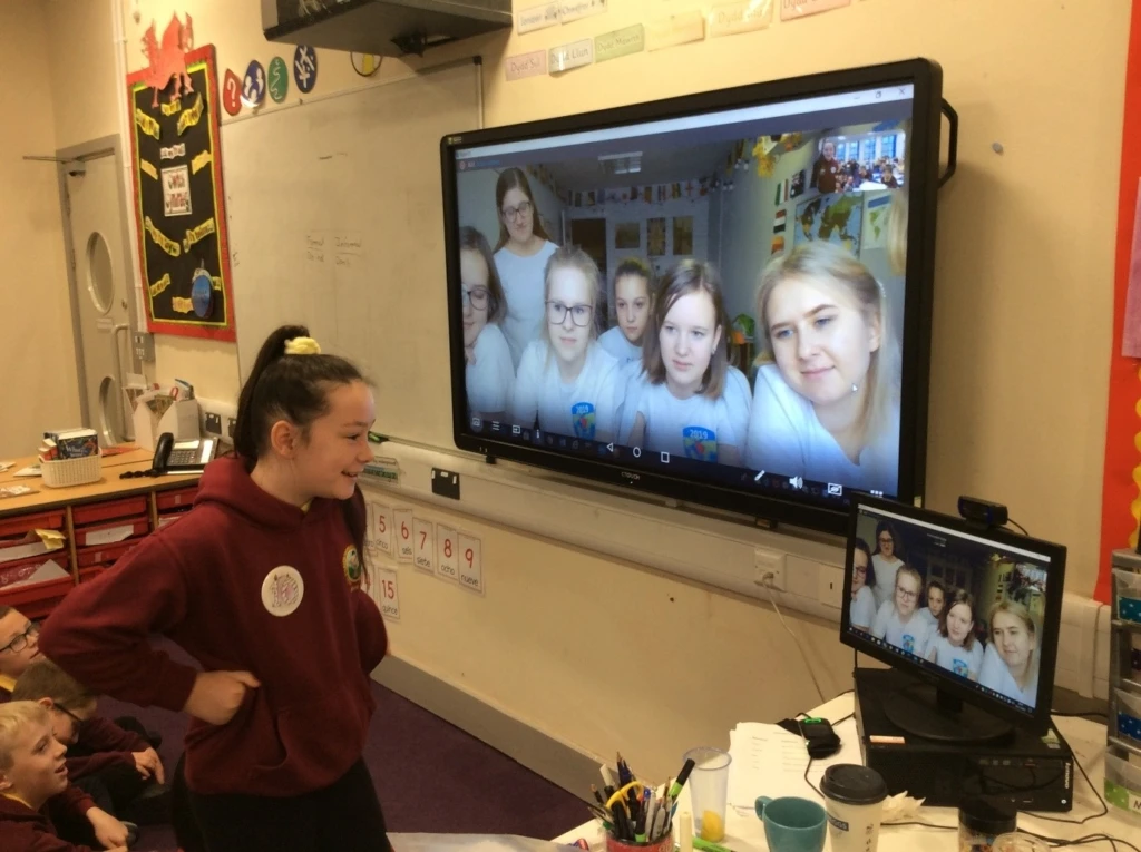 Darran Park Primary School students talk to Russian students on a TV screen via Skype. A girl stands in from of a laptop, facing a screen with five female students and a teacher on it.