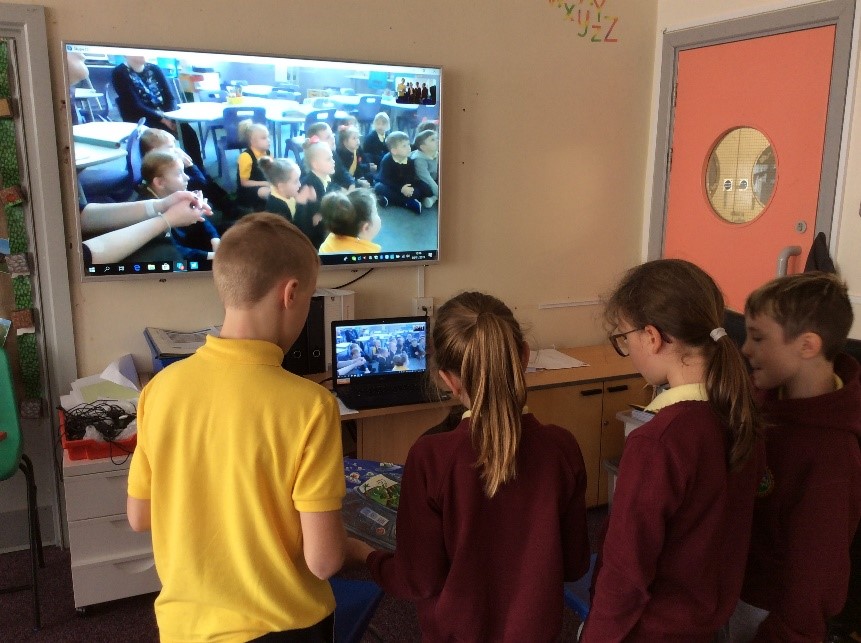 Darran Park Primary School students talk to other classes from around the world on Skype. A TV screen shows the students, while two girls and a boy face a laptop.