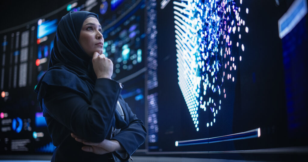 Female worker wearing a hijab analyses data on a large digital screen