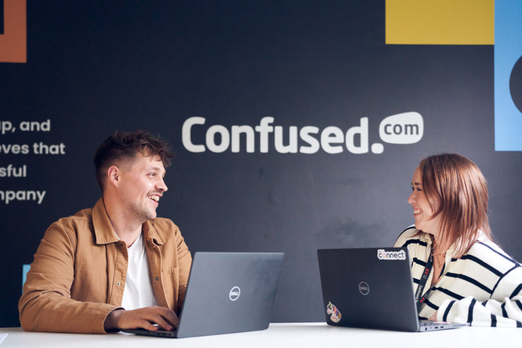 Smiling workers with laptops sit beneath a Confused.com logo