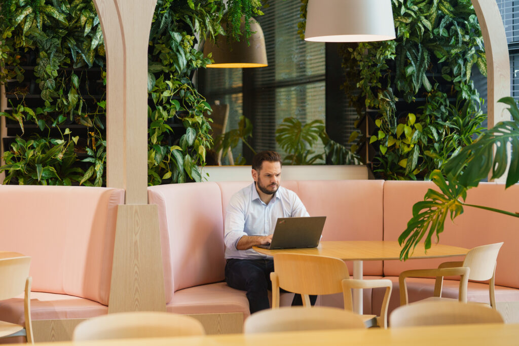 Male office worker works at a laptop amidst soft furnishings