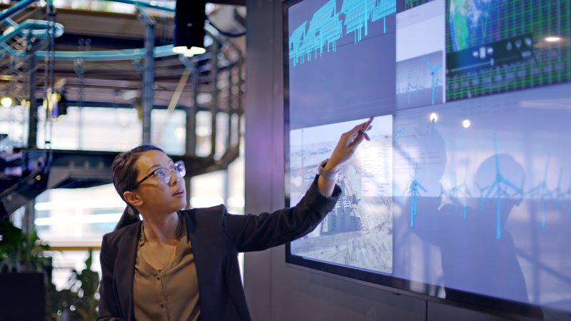 A female office worker points at a detail on a large touchscreen display