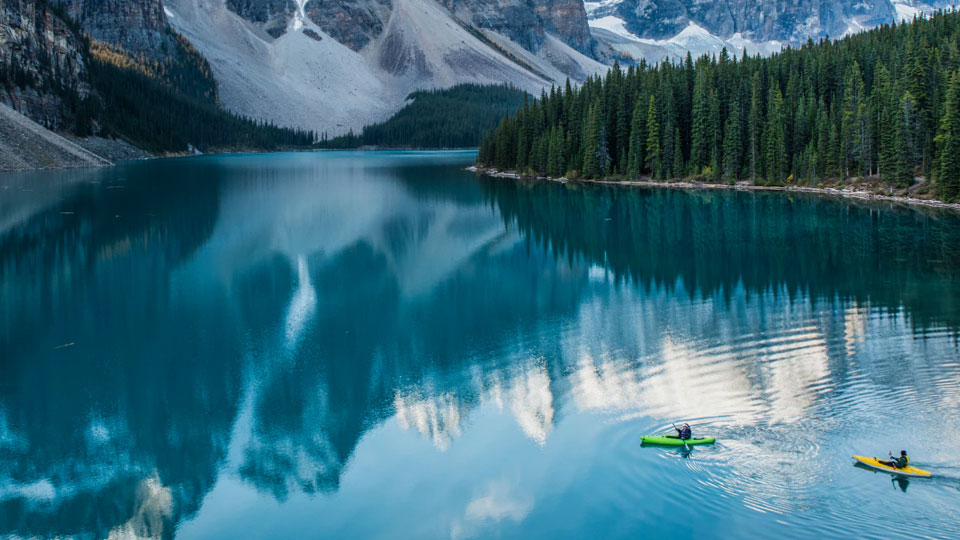 Two individuals kayaking across a lake in the middle of snowy mountains