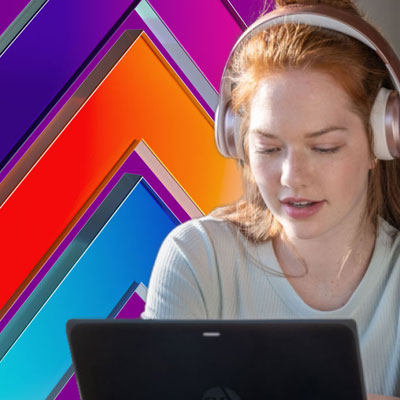 A student wears headphones and works on her laptop