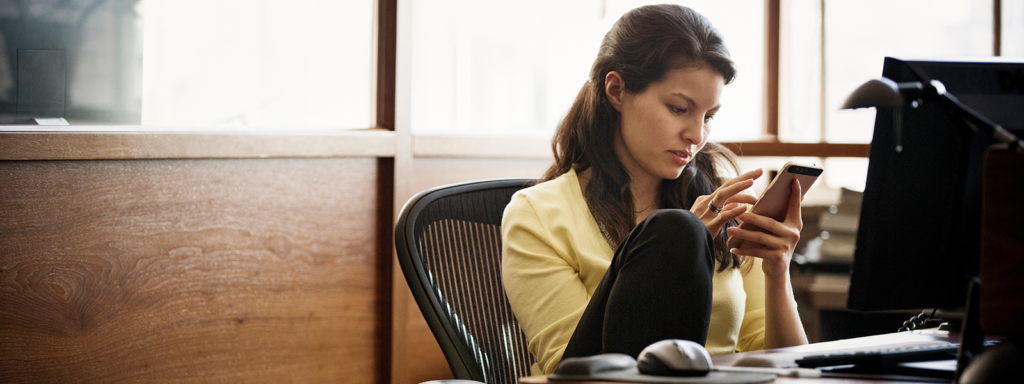 Image of a woman checking her phone while working at her desk.