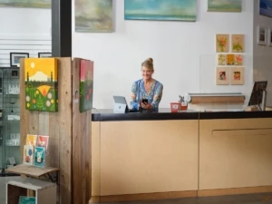 Retail shop owner working on Microsoft 365 Business Premium a mobile phone and a Surface. Female, retail, artwork, small business