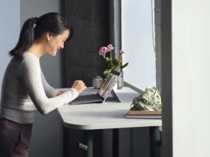 Adult female standing at her desk collaborating via Microsoft Teams video call on a Surface Pro 8 in laptop mode working on a Surface Pro Signature Keyboard.