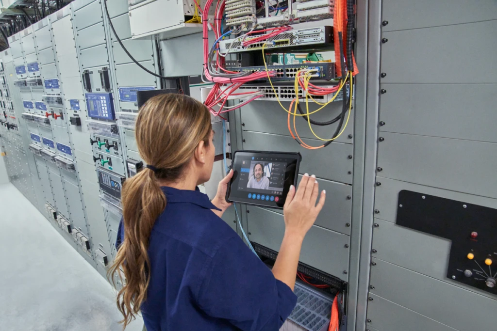 Field engineer inspects electrical substation server room on a wind farm using remote assist with a Surface tablet.