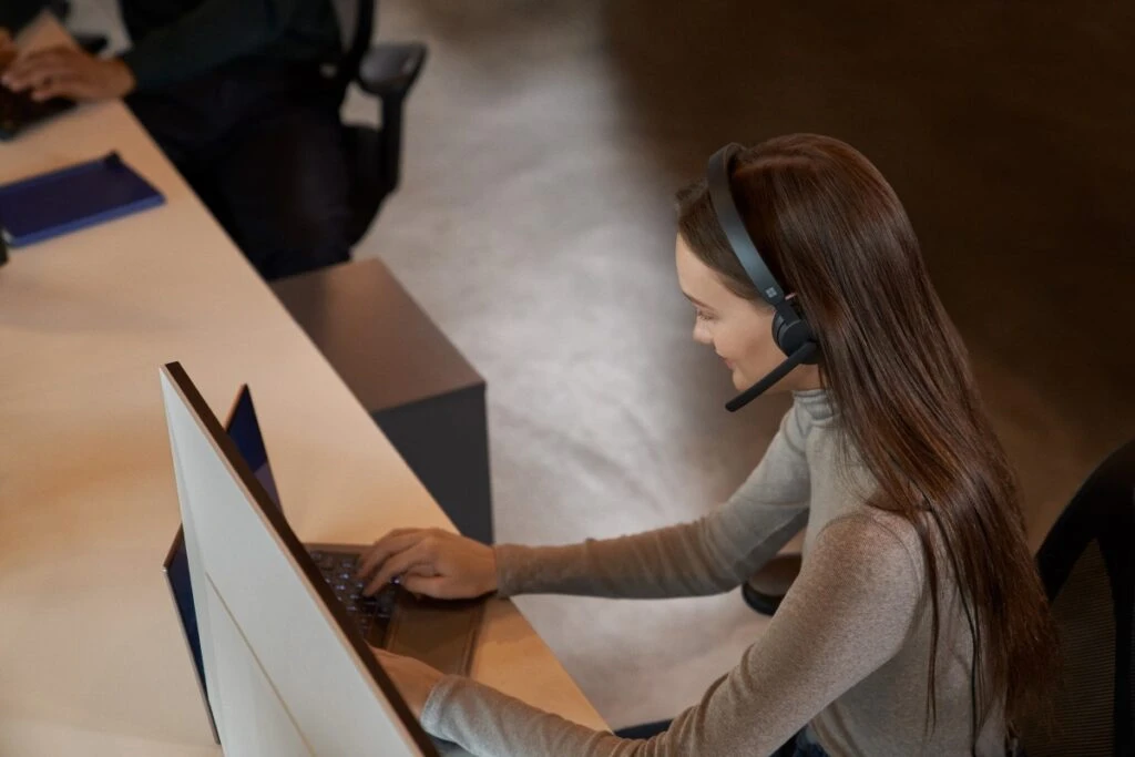 Customer service support call in action. Keywords: Dynamics 365; operations; woman; wearing headset; taking a phone call; typing