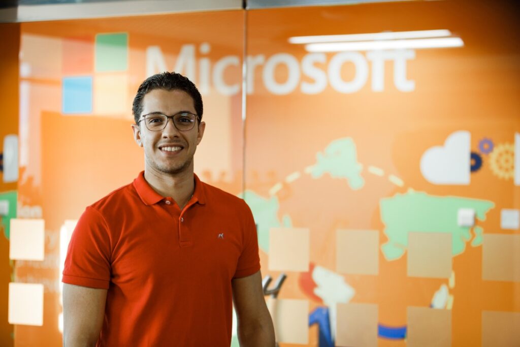 Close up portrait of male office worker standing in front of Microsoft wall display, smiling and looking directly at camera.