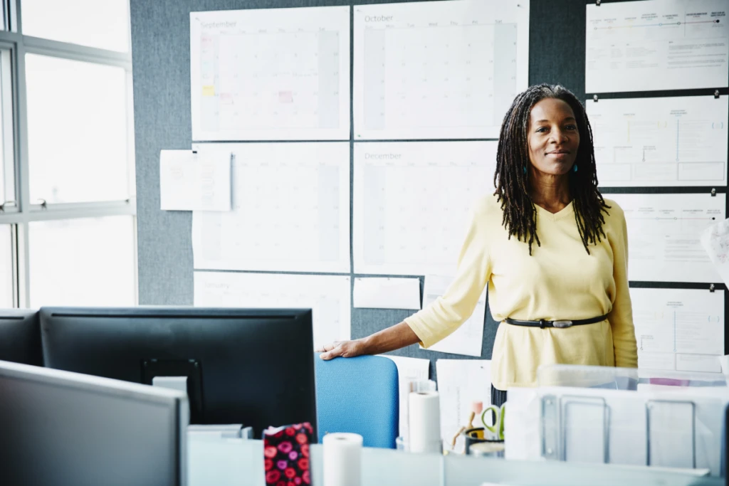 Smiling mature businesswoman standing at workstation in office.