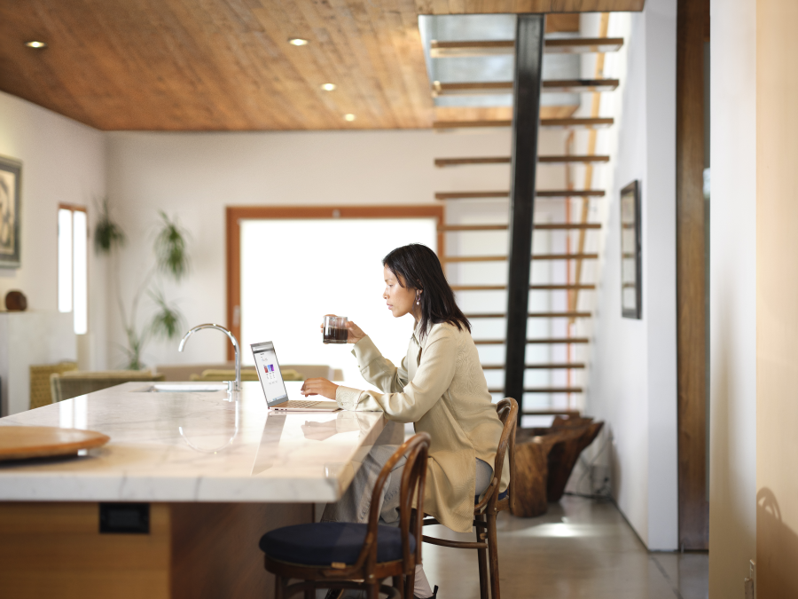 A woman sitting at a kitchen island with a cup of coffee in her hand, looking at a laptop