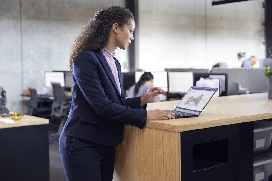 A woman standing at a table in an office, looking at a laptop.