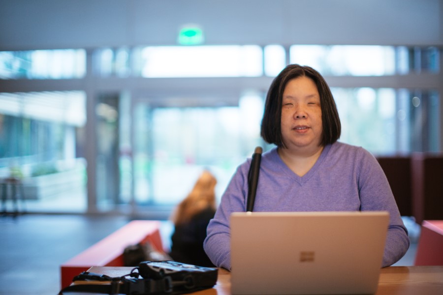 A woman who is blind works on a Surface device with a braille keyboard sitting on the side.