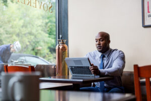 man in a suit sitting in a cafe restaurant using convertible laptop as tablet (screen not shown)