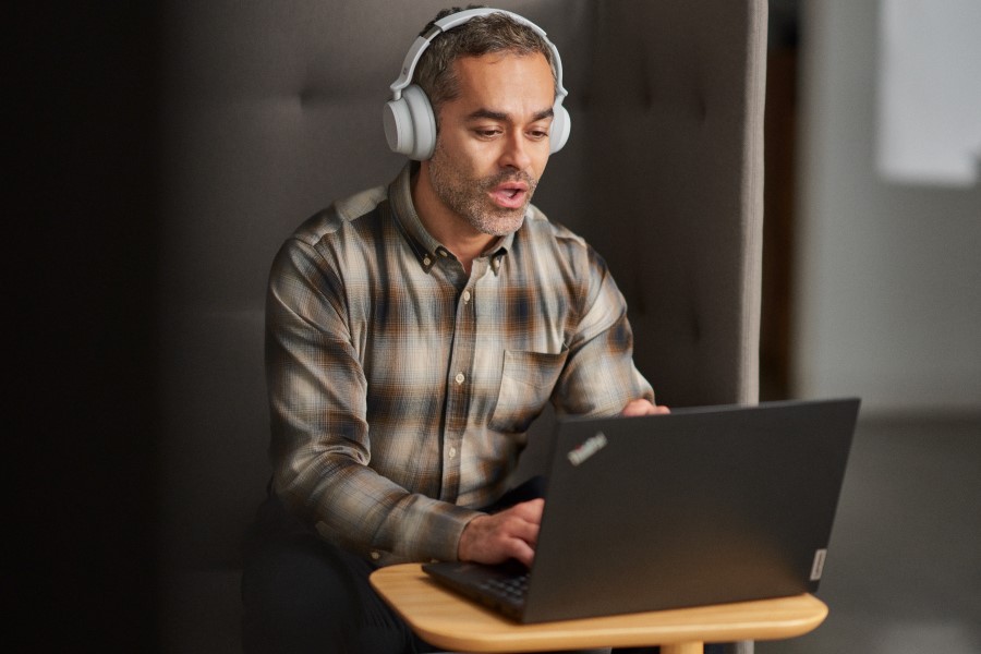 A man watching a webinar while using a cubicle in an open office setting​.