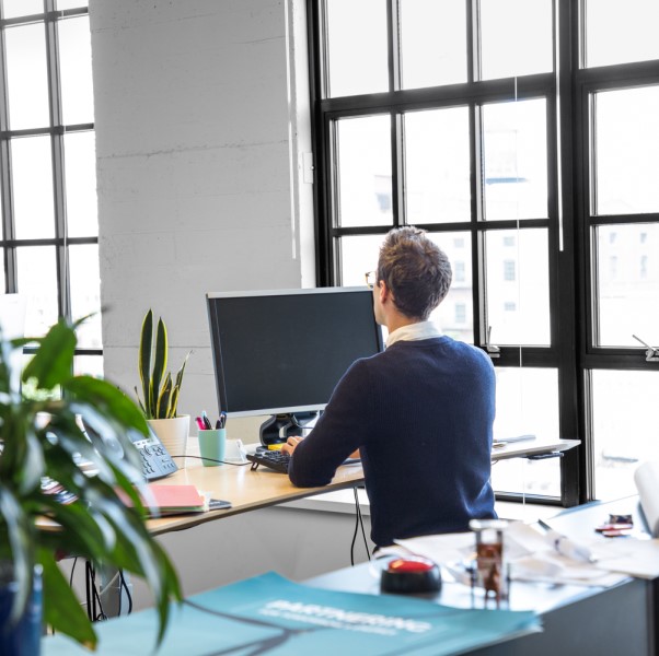 Male office worker standing at desk using desktop computer.