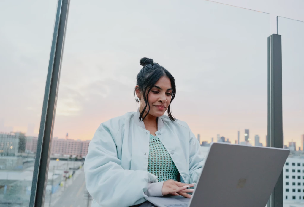 Microsoft 365 lifestyle photography of a female adult sitting outside typing on a Surface Laptop 5.