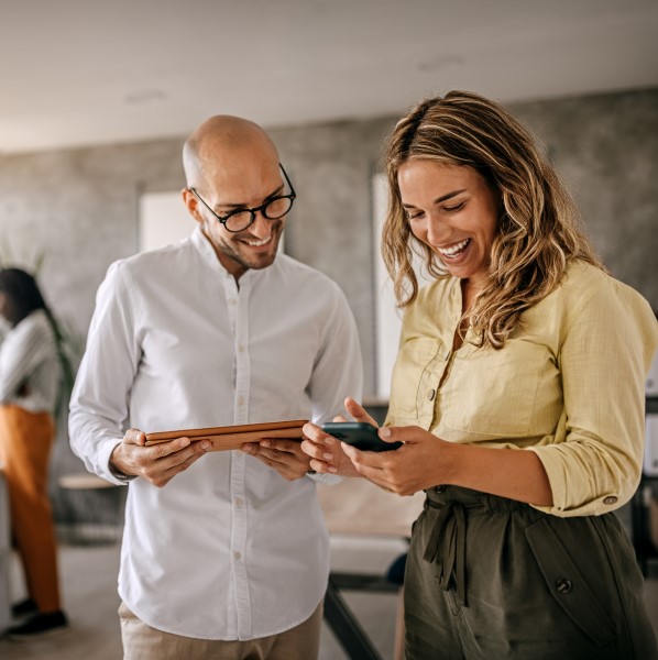 Cheerful female businesswoman standing with colleague looking at a digital tablet in a modern office space.