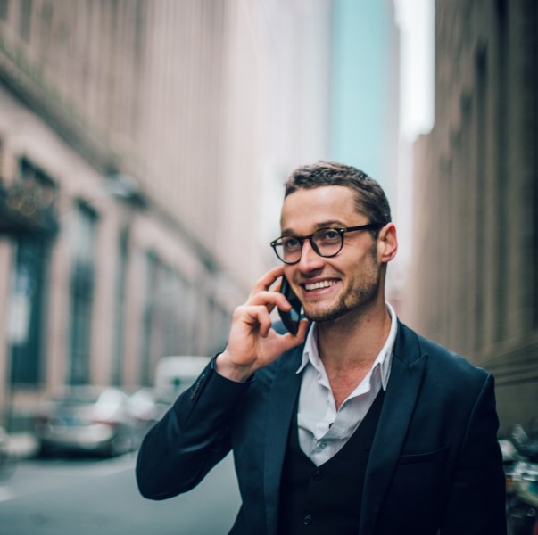 Businessman smiles as he talks on his mobile phone while walking down a street in the city.