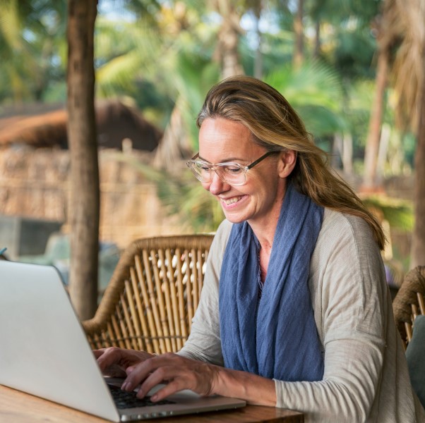 A smiling woman is working on her laptop at an outdoor cafe.