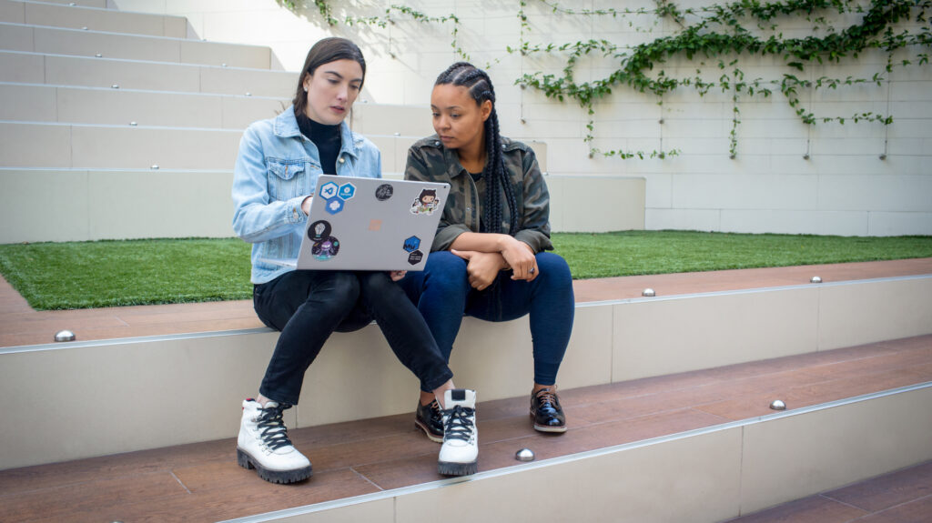 Two college students sitting on steps outside and working on a laptop together.