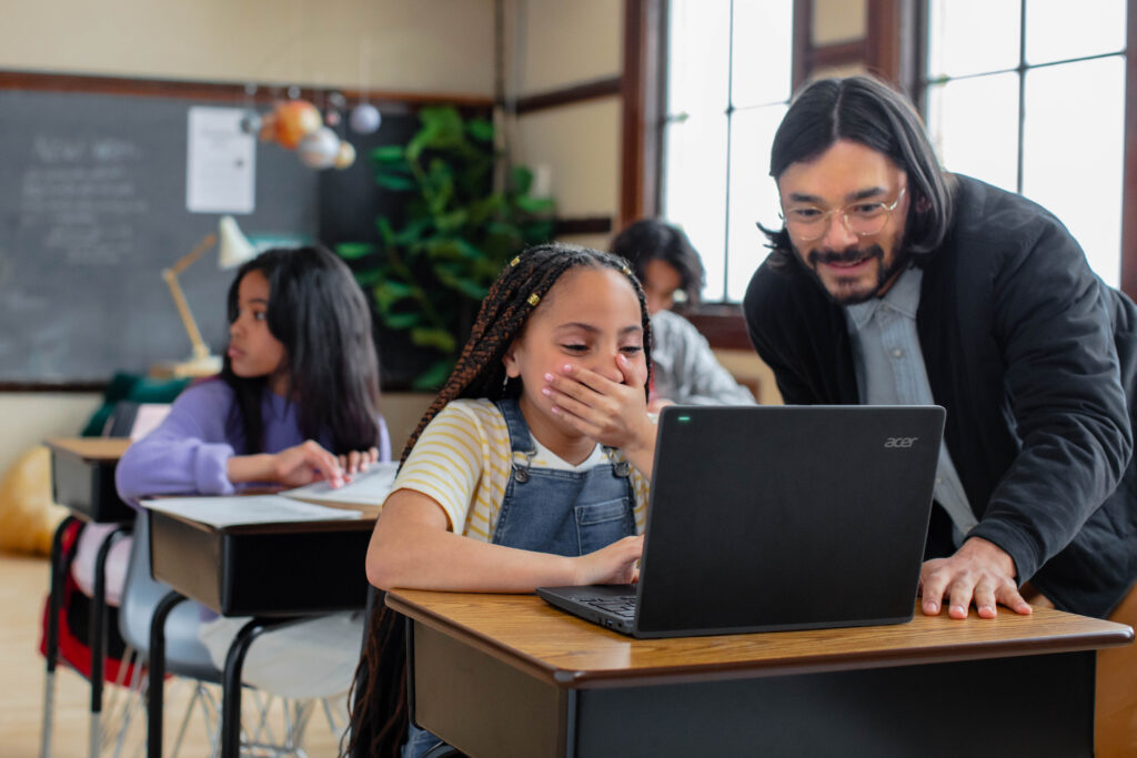 A teacher and a student looking at a laptop in a classroom setting.
