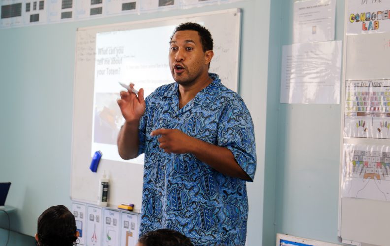 A man lectures at the front of a class.