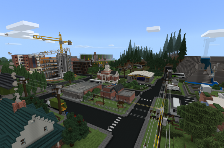 An aerial view of a city featuring a house, a building under construction, and a stand of evergreen trees in Minecraft: Education Edition